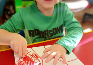 Uśmiechnięty chłopiec rysuje kredkami patriotyczny obrazek.