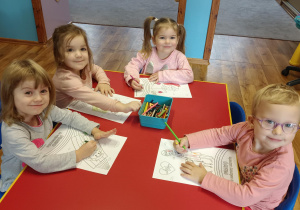 Cztery dziewczynki siedzą przy stoliku i kolorują kolorowanki na temat praw dziecka.