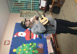 Pan z zespołu muzycznego prezentuje dzieciom grę na ukulele.