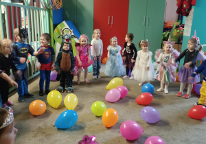 Dzieci przebrane za postacie z bajek, tańczą stojąc w półokręgu. Przed dziećmi leżą kolorowe balony.