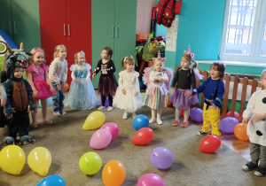 Dzieci przebrane za postacie z bajek, tańczą stojąc w półokręgu. Przed dziećmi leżą kolorowe balony.