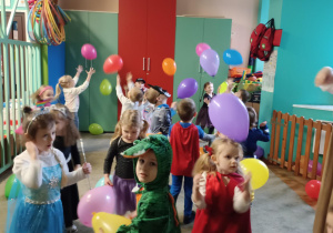 Dzieci przebrane za postacie z bajek podrzucają kolorowe balony.