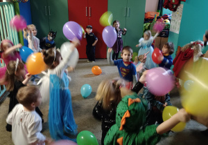 Dzieci przebrane za postacie z bajek podrzucają kolorowe balony.
