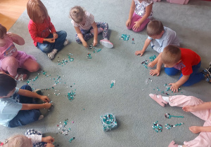 Dzieci siedzą na dywanie układają różne wzory z guzików .
