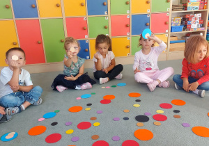 Dzieci siedzą na dywanie a przed nimi są kolorowe kropki.