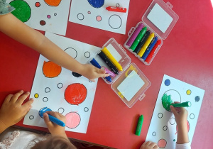 Dzieci przy stolikach kolorują kropki.