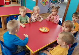 Dzieci siedzą przy stole i częstują się słodkościami.