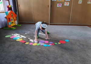 Chłopiec układa kolorowe, różnej wielkości koła na dywanie wg włassnego pomysłu.
