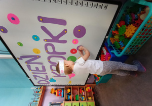 Dziewczynka ozdabia tablicę z napisem "Dzień Kropki" kolorowyki kołami wg własnego pomysłu.