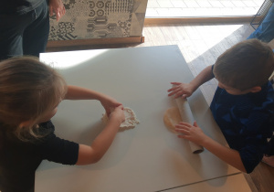 Dzieci przy stole wyrabiają ciasto drożdżowe na bułeczki.