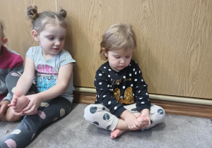Dziewczynki siedzą na dywanie i masyją swoje stópki.