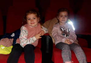 Dwie dziewczynki siedzą w fotelach kinowych.