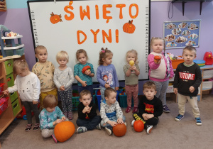 Dzieci pozują na tle napisu "Święto Dyni". Niektóre trzymają różnej wielkości dynie.