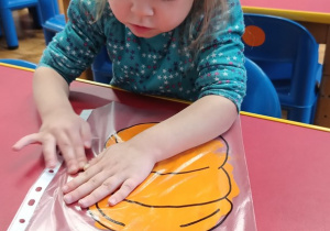 Dziewczynka rączkami rozprowadza farbę aby wypełnić kontury dyni.