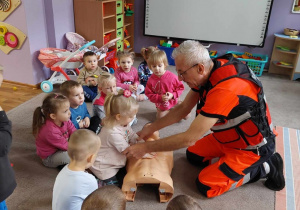 Ratownik medyczny, na manekinie pokazuje dziewczynce jak wykonać masaż serca.