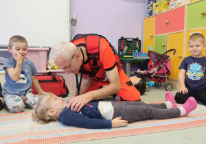 Ratownik medyczny demonstruje dzieciom jak pomóc poszkodowanemu.