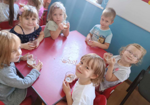 Dzieci siedzą przy stolikach i piją własnoręcznie wykonany sok z jabłek.