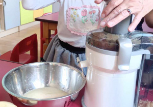 Dziewczynka robi sok z jabłek przy pomocy sokowirówki.