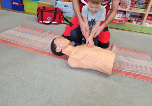 Chłopiec w asyście ratownika wykonuje na manekinie masaż serca.