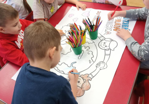 Dzieci z trzeciego stolika wspólnie kolorują mega kolorowankę.