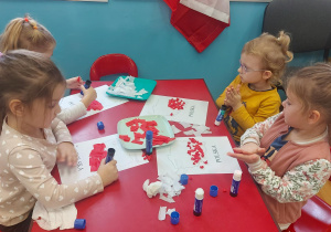 Dzieci przy stolikach wykonują pracę plastyczną. Wyklejaja kontur Polski białą i czerwoną bibułą.