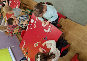 Dzieci siedzą przy stolikach i wykonują kotyliony.