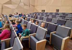 Dzieci siedzą na widowni na auli w Szkole Muzycznej.