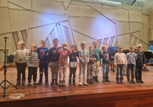 Dzieci pozują do zdjęcia stojąc na scenie w Szkole Muzycznej.