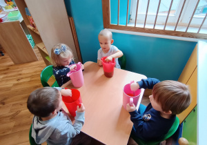 Dzieci siedzą przy stoliku i mieszają galaretkę aż się rozpuści.