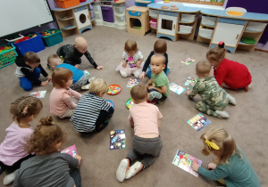 Dzieci siedzą w rozsypce na dywanie. Każde z nich ma swój obrazek i próbuje znajeźć właściwe figury.