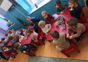 Dzieci siedzą przy stolikach, na których stoją słoiki z przeróżnymi ziołami.