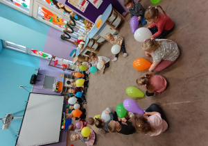 Dzieci siedzą w kole i trzymają swoje balony.