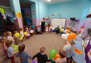 Dzieci trzymają się za ręce i tańczą z balonami po kole.