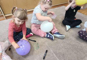 Dziewczynki siedzą na dywanie i ozdabiają swoje balony naklejkami.
