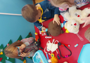 Dzieci siedzą przy stolikach i bawią się w lekarzy swoich misiów.