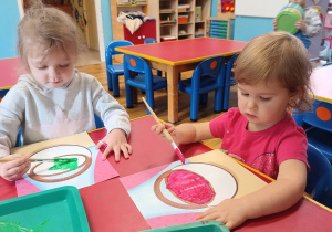 Dwie dziewczynki malują farbami koszyk na warzywa.