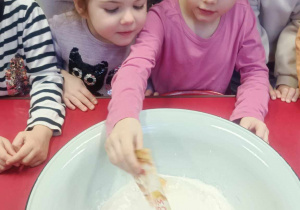 Dziewczynka wsypuje składnik ciasta - cukier waniliowy.