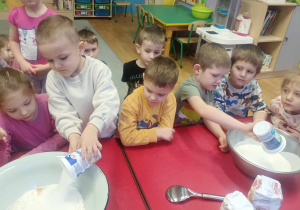 Chłopcy wsypują mąkę do mis z ciastem.