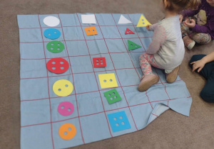 Dziewczynka kładzie guzik w kształcie trójkąta we właściwym miejscu na macie do kodowania.