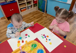 Dzieci dmuchają przez słomkę na krople farby, rozdmuchując ją tak, aby powstał kleks.