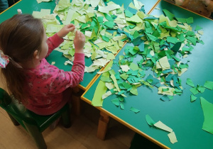 Dzieci przy stoliku drą zielone kartki na mniejsze kawałki
