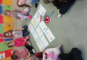 Dzieci siedzą na dywanie, rozłożone są ilustracje dotyczące higieny jamy ustnej oraz model szczęki i szczoteczka.