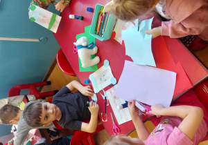 Dzieci siedzą przy stoliku i wykonują niedźwiedzia z torebki papierowej.