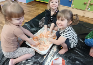 Szczęśliwe dziewczynki podczas mieszania mąki pszennej z wodą i pomarańczową farbą.