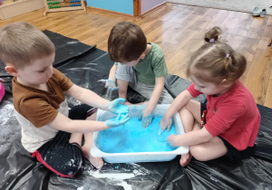 Dzieci bawią się niebieską cieczą nienewtonowską wykonaną z mąki ziemniaczanej.