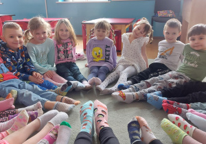 Dzieci siedzą w kole z wyciągniętymi nogami i pokazują swoje kolorowe skarpetki nie do pary. Ujęcie 1