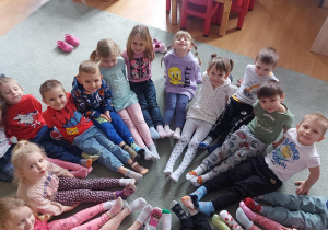 Dzieci siedzą w kole z wyciągniętymi nogami i pokazują swoje kolorowe skarpetki nie do pary. Ujęcie 2