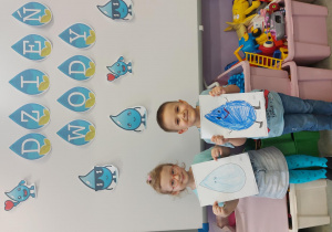 Dziewczynka i chłopiec pozują do zdjęcia ze swoimi pracami które przedstawiają krople wody.