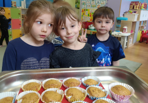 Dwie dziewczynki i chłopiec stoją przed własnoręcznie upieczonymi marchewkowymi muffinkami .