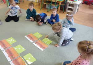 Dzieci siedzą w kręgu na dywanie i dopasowują ilość kropek na kartonikach do ilości marchewek.